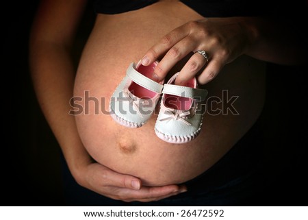 mother holding pair of baby shoes over belly while cradling stomach with other hand