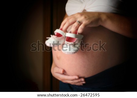 mother holding pair of baby shoes over belly while cradling stomach with other hand
