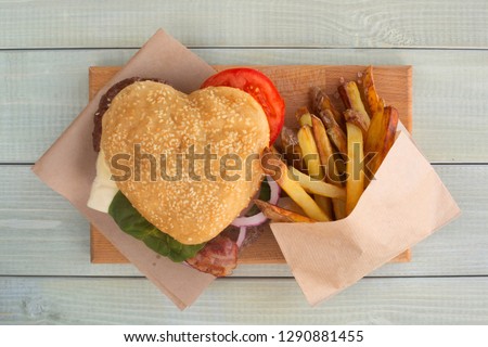 Heart shaped hamburger and french fries, love burger fast food concept, Valentines day surprise dinner, wooden background, top view flat lay