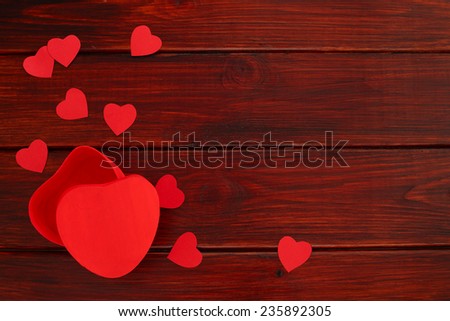 Valentines day gift box shaped as heart and paper hearts on wooden background