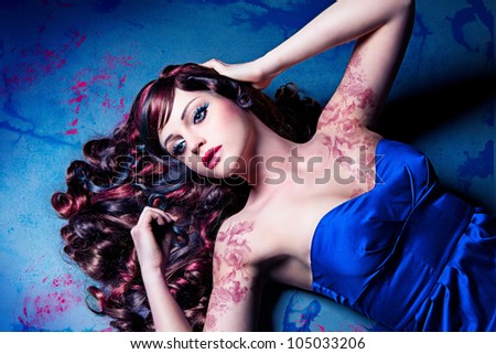 girl with beautiful colored curly hair lying on a painted floor like a doll