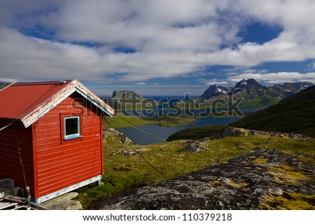 Picturesque panorama on Lofoten islands with red mountain cabin, fjords and high mountain peaks surrounding them