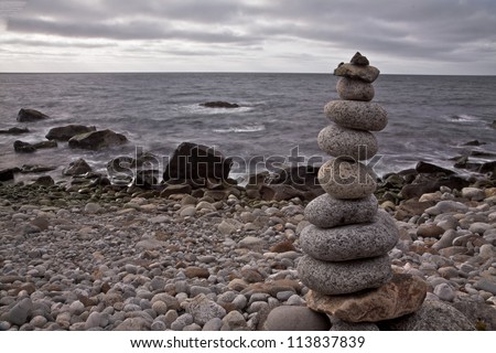 Rounded stones piled up on each other forming small statue on rocky beach in arctic Norway