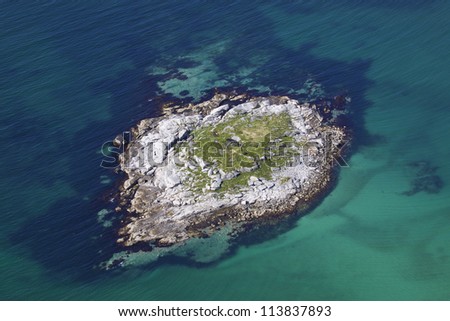Aerial view of small rocky island in turquoise sea near norwegian coast