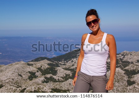 Smiling young girl on hilltop with beautiful panorama of nature park Biokovo on Dalmatian coast near Makarska Riviera in Croatia in the background