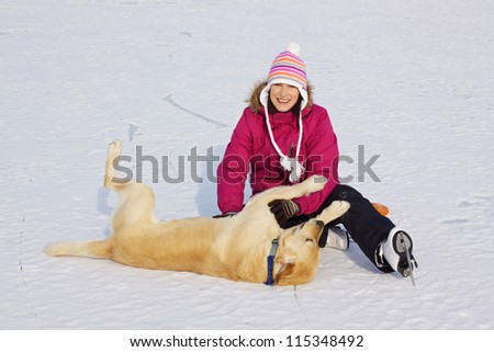 Joyful attractive girl with ice skates playing with her dog on frozen lake