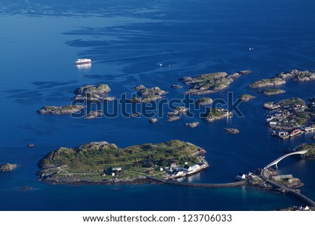 Large cruising ship passing by picturesque tiny islands on norwegian coast connected by bridges near town of Henningsvaer on Lofoten islands