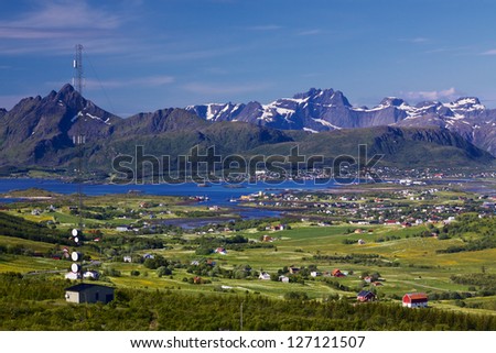 Scenic panorama with green meadows, town of Leknes and snowy peaks of picturesque Lofoten islands in Norway