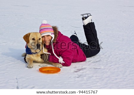 Girl with ice skates laying on the ice of frozen lake with her dog