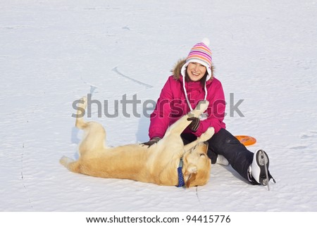 Girl with ice skates having fun with her dog on frozen lake