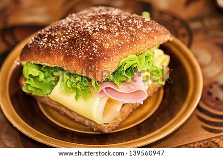 Healthy sandwich with lettuce, cheese and ham on a brown plate and background