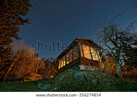 Small house with big orange windows and a bright starry night sky. Sweden