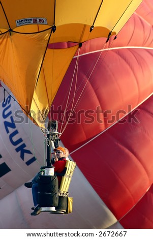 Balloonists sitting on a chair type gondola with colorful hot air balloons as background