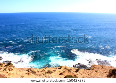 Looking down from a cliff top where the horizon meets the blue sea with waves and white caps