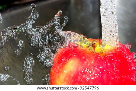 Apple being washed under a tap with water splashing from it