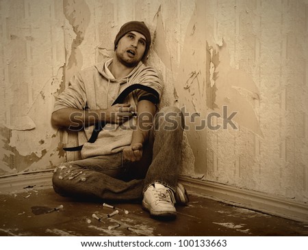 stock photo : bad man - addict  with a syringe using drugs  sitting on the floor