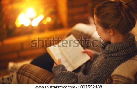 young woman enjoys reading a book by the fireplace on a winter evening