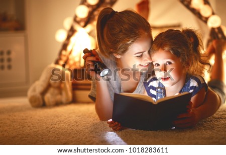 reading and family games in   tent. mother and child daughter with  book and flashlight before going to bed