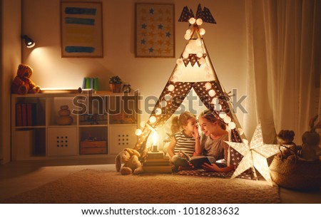 reading and family games in   tent. mother and child daughter with  book and flashlight before going to bed