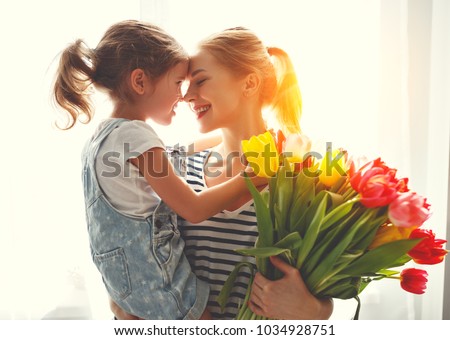 happy mother\'s day! child daughter congratulates mother and gives a bouquet of flowers to tulips