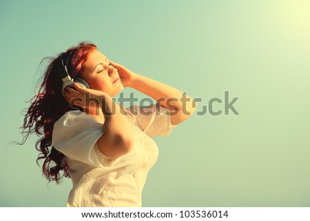 beautiful redhead girl with long hair enjoys music with headphones in the sky with your eyes closed