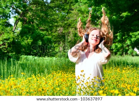 beautiful girl in headphones enjoying the music with flowing hair in a field of flowers in nature