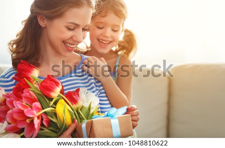 happy mother\'s day! child daughter congratulates mother and gives a bouquet of flowers to tulips and gift