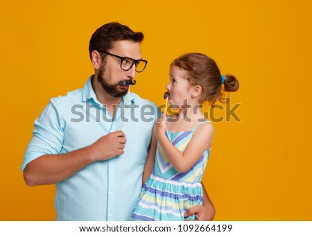 happy father\'s day! funny dad and daughter with mustache fooling around on colored yellow background