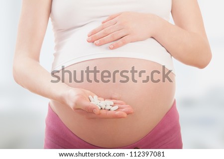 belly of pregnant woman and vitamin pills in the hand