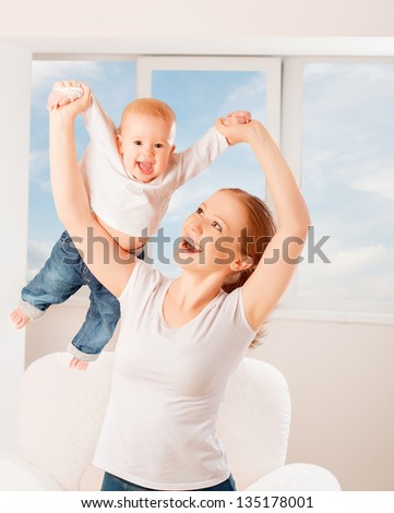 Mother and baby are playing active games do gymnastics and laughing at home against the window and the sky Mother and baby are playing active games do gymnastics and laughing at home against the window and the sky