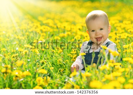 Beautiful happy little baby girl sitting on a green meadow with yellow flowers dandelions on the nature in the park