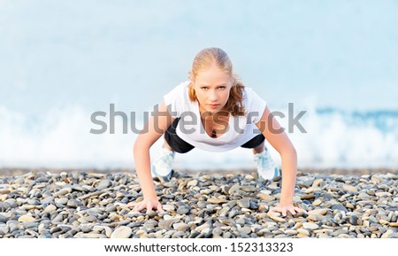 Young healthy woman playing sports push-ups outdoors on the beach, facing the sea