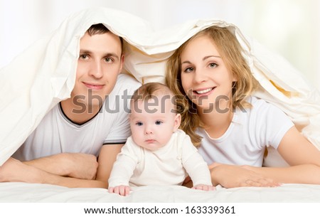 happy family in bed under a blanket. mother, father, baby