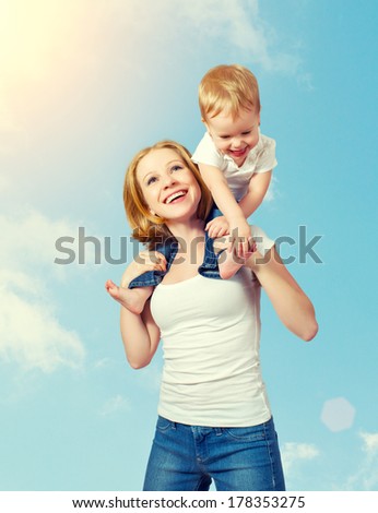 happy family. baby sits astride the shoulders of the mother and laughing on blue sky background