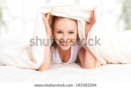 funny beautiful young blond woman under the blanket in the bed