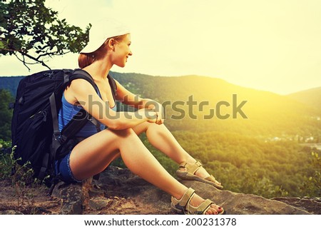 woman tourist with a backpack sitting, resting on a mountain top on a rock on the nature of the journey