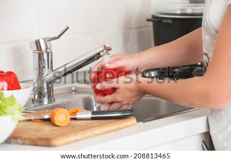 washing vegetables. woman washing red pepper under the tap