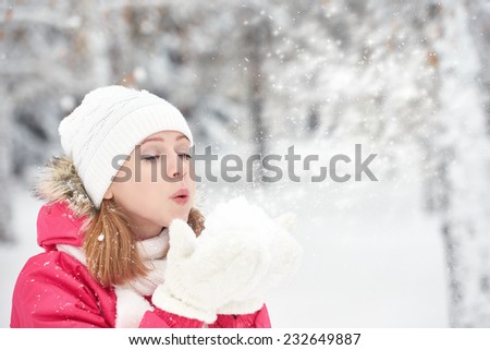 happy girl on a frosty winter walk on the street blows snow from hands