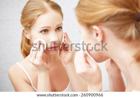 beautiful young woman removes makeup with face skin cotton pad in the mirror