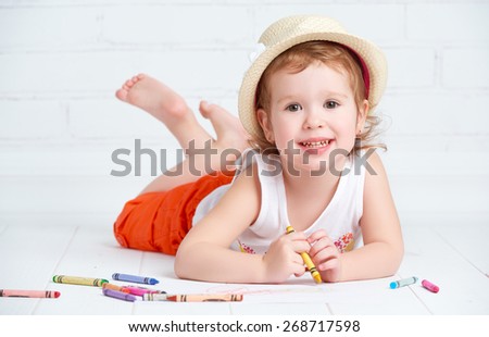 happy little artist  girl in a hat draws pencil lying on the floor