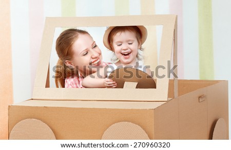 Happy family mother and little daughter ride on toy car made of cardboard on vacation