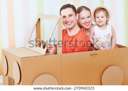 Happy family mother, father, daughter ride on toy car made of cardboard on vacation