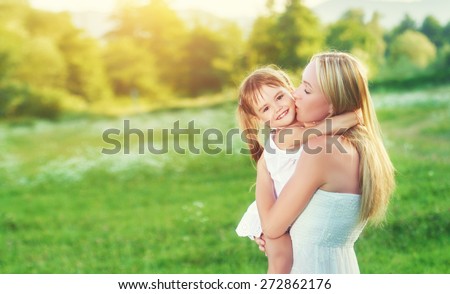 happy family on nature outdoors mother kissing little daughter on the green meadow