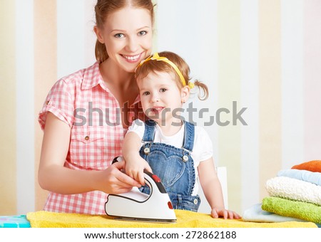 happy family mother and baby daughter together engaged in housework iron clothes iron