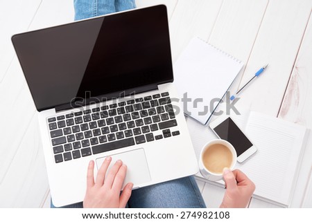 happy young woman in jeans and relaxes at home working at a laptop with a cup of coffee