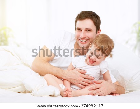 Happy family father and baby child daughter playing in bed