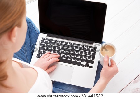 happy young woman in jeans and relaxes at home working at a laptop with a cup of coffee