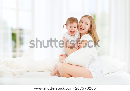 The happy family mother and baby daughter playing and laughing baby kissing in bed
