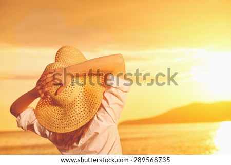 beauty happy woman in her hat is back and admire the sunset over the sea on the beach