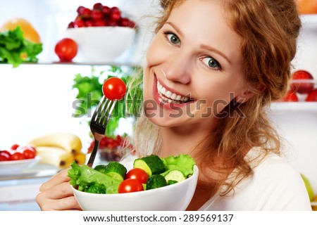 happy woman eats healthy food vegetable vegetarian salad about refrigerator